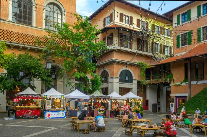 Several street food stalls are set up in the courtyard of the One Nimman shopping complex, where diners sit at picnic tables enjoying their meals.