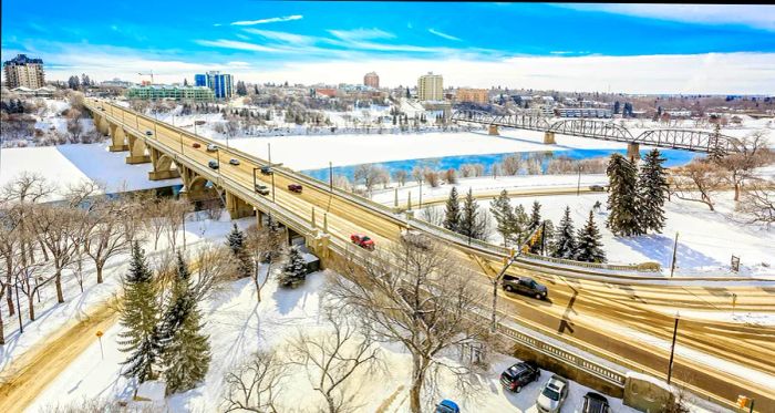 A winter view of a riverside city blanketed in snow, with roads and bridges covered.