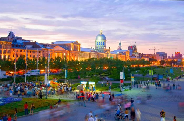 A bustling crowd gathers in an open square before a grand municipal building at dusk.