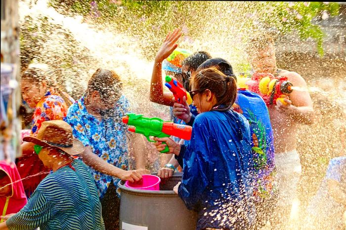 A group of people gathered together, joyfully spraying and splashing water at each other, with droplets flying all around them.