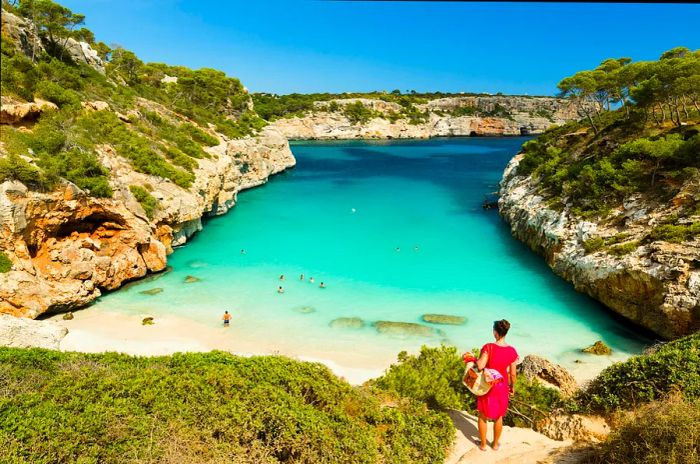 A woman in a red cover-up gazes out over a breathtaking beach in Mallorca.