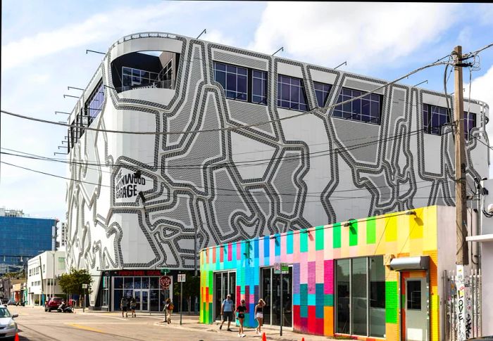 The exterior of a building showcases a unique grey-and-white pattern, contrasting with a nearby low-rise structure featuring vibrant blocks of color.