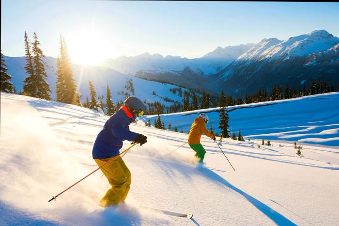 Skiers glide down a powdery slope amidst a sun-drenched mountainous landscape.