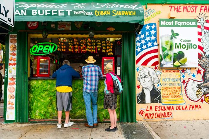 Three patrons are ordering from the open-air counter of a restaurant serving Cuban cuisine and beverages on historic Calle Ocho in Little Havana, Miami.