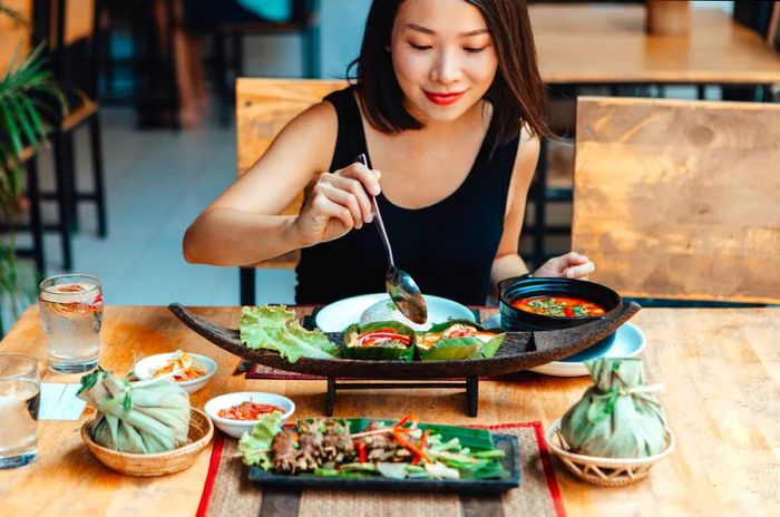 A close-up view of a young Asian woman enjoying authentic Thai cuisine at a restaurant.