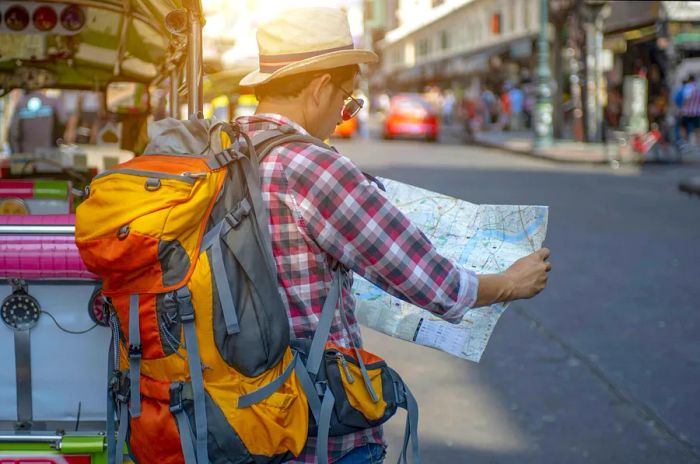 A man with a backpack studies a map while navigating a bustling street in Bangkok.