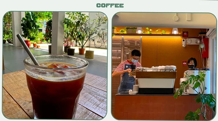 A glass of iced coffee with a straw, while two baristas prepare drinks at the coffee counter