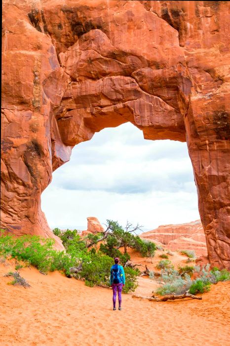 A female hiker admires the Pine Tree Arch at Devils Garden in Arches National Park.