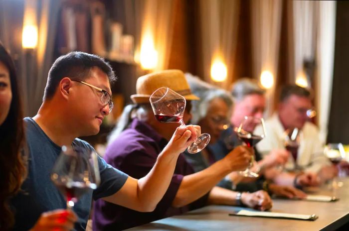 Patrons in a wine tasting room observe the wine in their glasses at the bar.