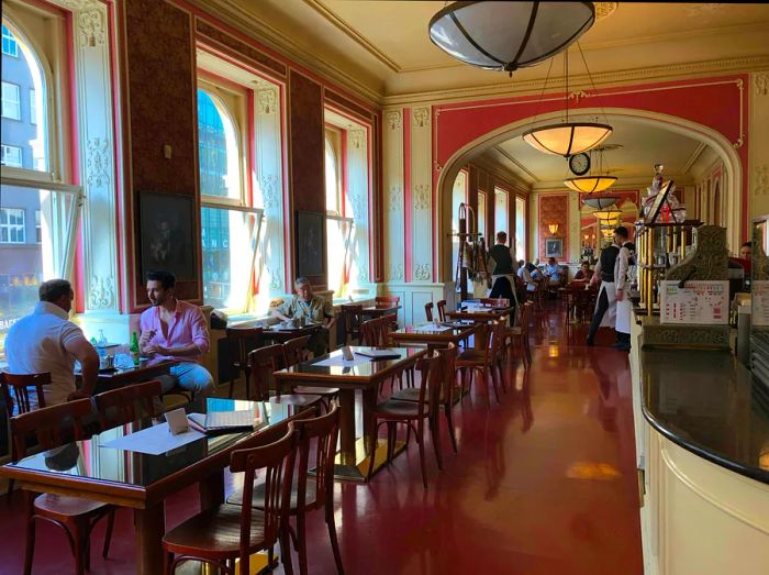 Guests enjoying their time inside Café Louvre, adorned with high ceilings and Parisian-style decor