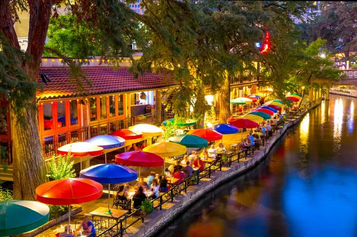 Vibrant umbrellas line a waterway with diners enjoying their meals nearby