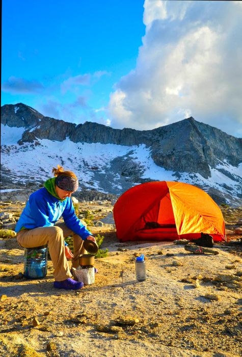 A woman relaxing beside a pitched tent in the snow-capped Sierra Nevada.