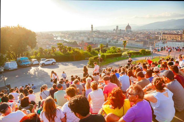 Groups of people gather to watch the sunset over the city skyline, while a car blocks another nearby.