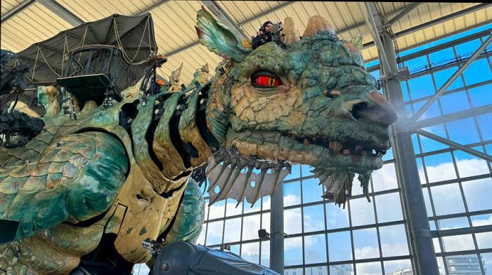 A gigantic mechanical dragon, maneuvered by a pilot using levers and pedals, resides in its transparent hangar.