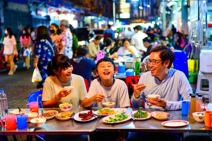 A family enjoying street food amidst the bustling crowd on Yaowarat Road in Bangkok