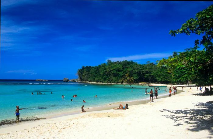 Visitors relaxing on the white sandy shores and swimming in the clear waters at Winnifred Bay in Port Antonio, Jamaica.