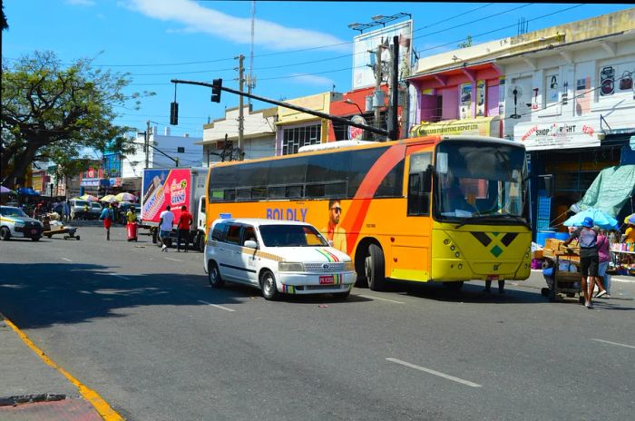 A vibrant yellow bus, a taxi, and commuters bustling through a street in downtown Kingston