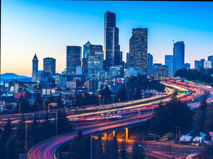 A long exposure captures Interstate 5 alongside the Seattle skyline at dusk.