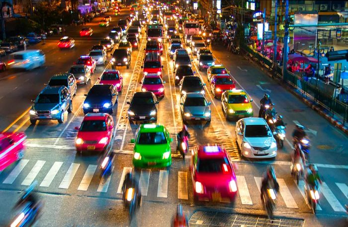 A line of brightly-colored taxis in green, yellow, and pink waits at a junction in Bangkok during the night.