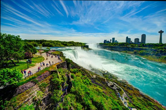 A series of cascading waterfalls flows alongside a river, where visitors follow a path to reach a closer viewpoint.