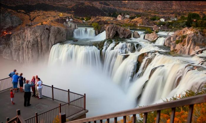 Visitors snap photos on a platform overlooking a waterfall featuring multiple cascades.