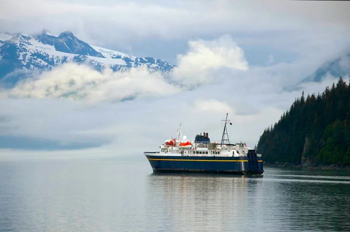 A large ferry departs from a port framed by mountains shrouded in clouds