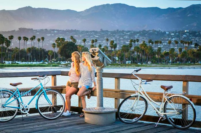 Two women enjoying a bike ride on a Santa Barbara pier at sunset