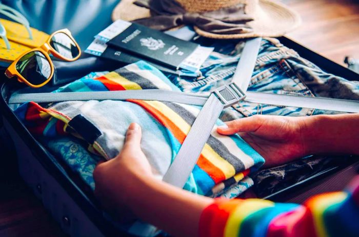 A woman’s hands packing a vibrant sweater into a suitcase at home