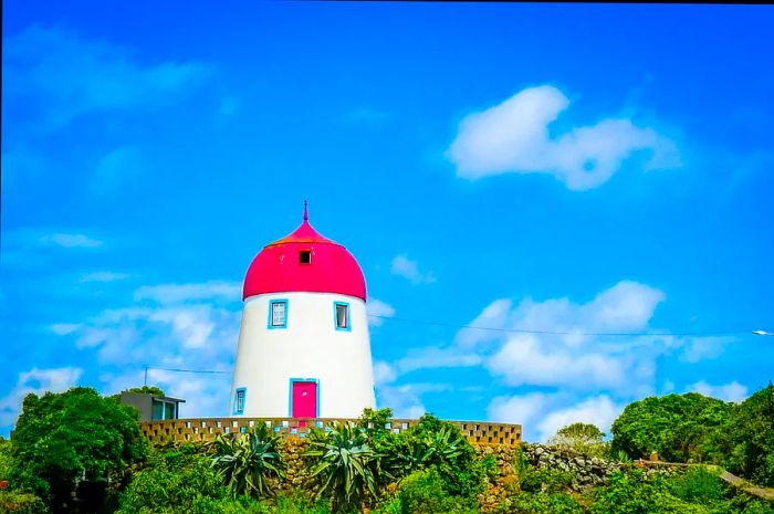 A red-roofed, Dutch-style windmill stands against a clear blue sky, though its sails are missing.