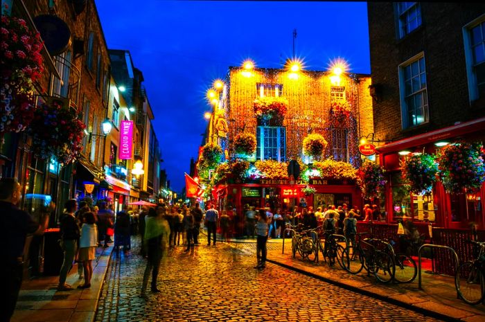 People enjoying the nightlife on a cobblestone street outside several pubs in the city