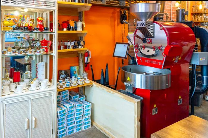 A cabinet next to a large red coffee grinder showcases espresso cups and coffee-themed trinkets for sale.