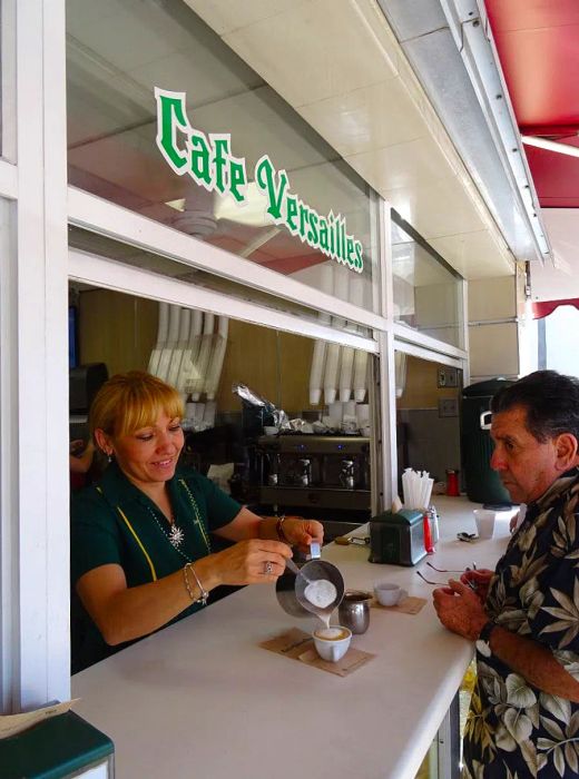 A woman hands over coffee to a customer from the ventanita at Café Versailles, Miami