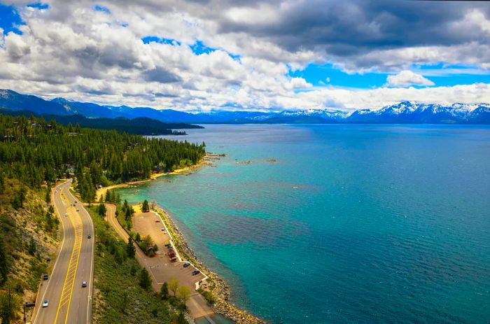 A road and parking area next to a large lake surrounded by mountains