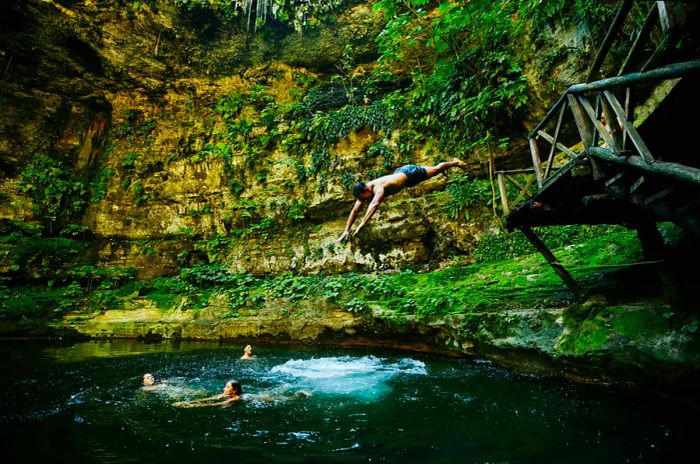 A man dives into a cenote—a sunken water hole—to join friends swimming there