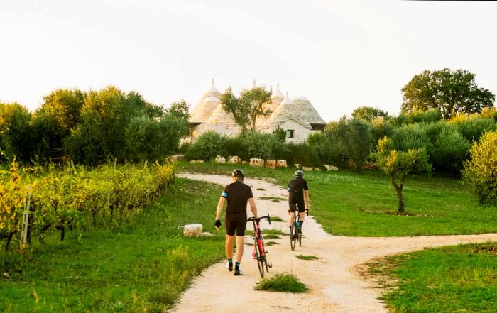 Two cyclists walk their bikes along a path leading to conical white limestone structures.