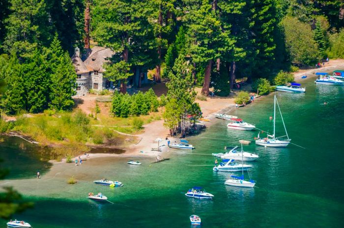 Small boats are moored in a bay in front of a Scandinavian-style mansion surrounded by lush woods.