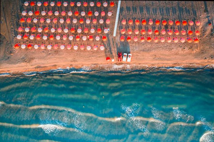 Aerial view of sunshades on a sandy beach kissed by waves