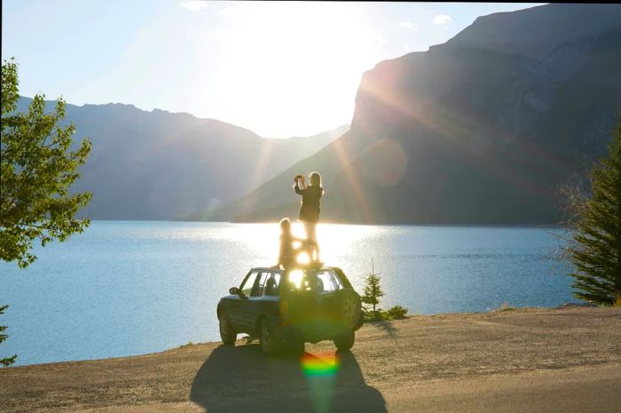 A woman captures a moment from the roof of a car while a man enjoys the serenity of a lake in Banff National Park, Alberta, Canada.