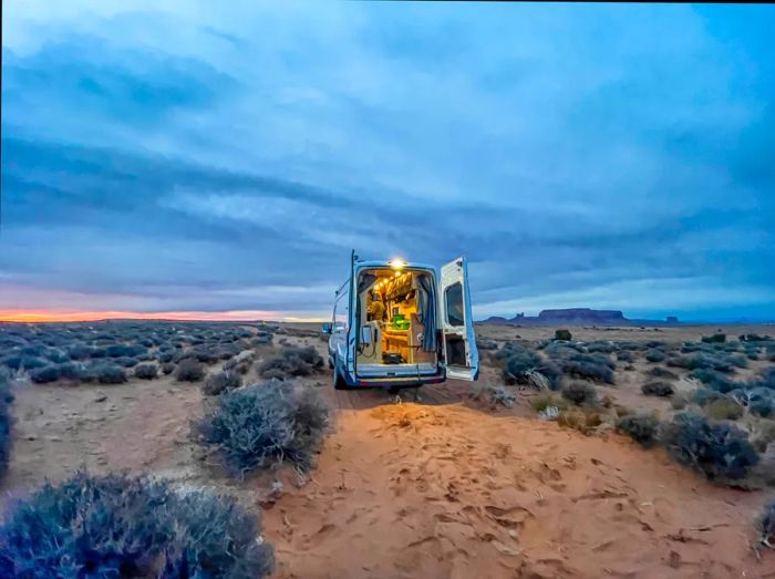 A camper van with its rear doors open, set against the backdrop of the Monument Valley Desert, straddling Utah and Arizona, USA