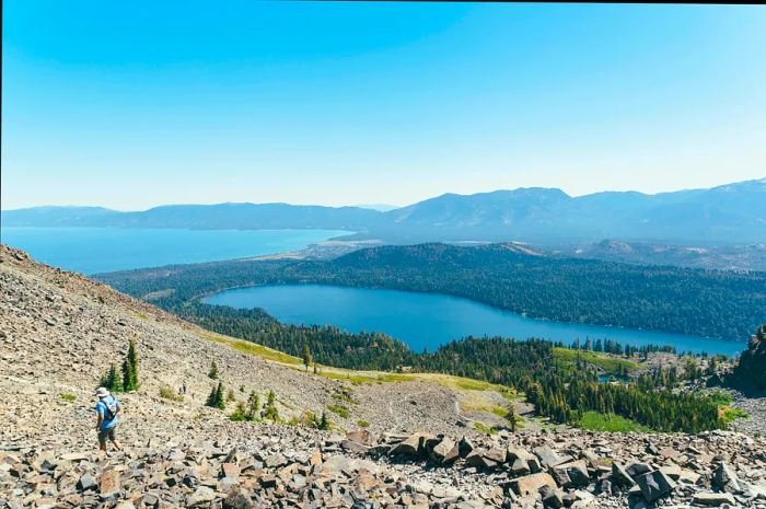 A hiker navigates a steep, rocky path overlooking a lake