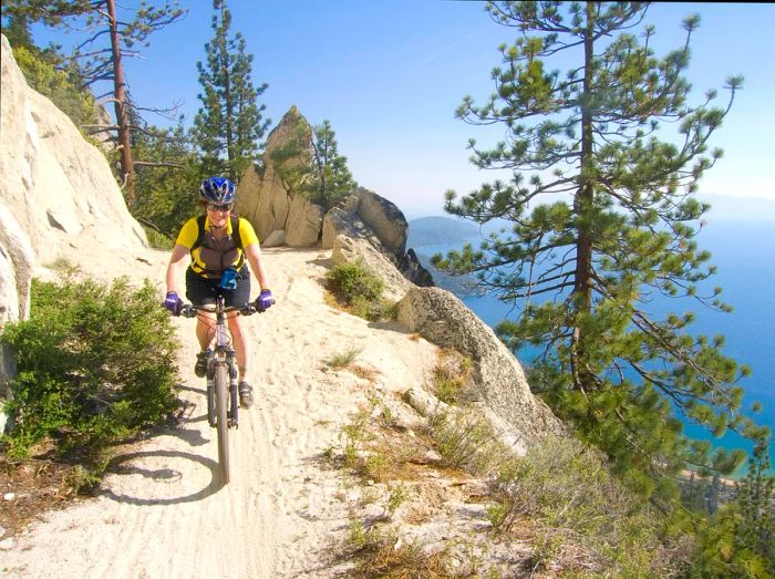 A woman riding a mountain bike beams as she navigates a steep sandy trail