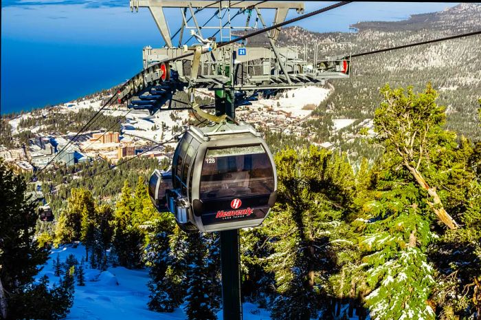 A cable car making its way up a mountain, with a large lake in the background.