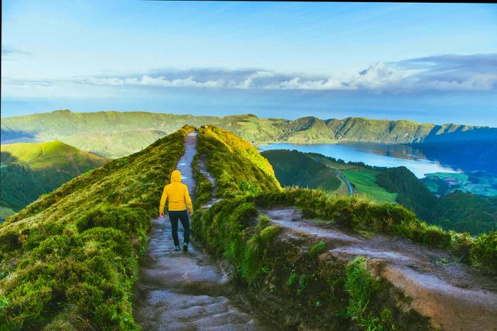 A person in a yellow rain jacket strolls down a path flanked by two craters filled with lagoons.