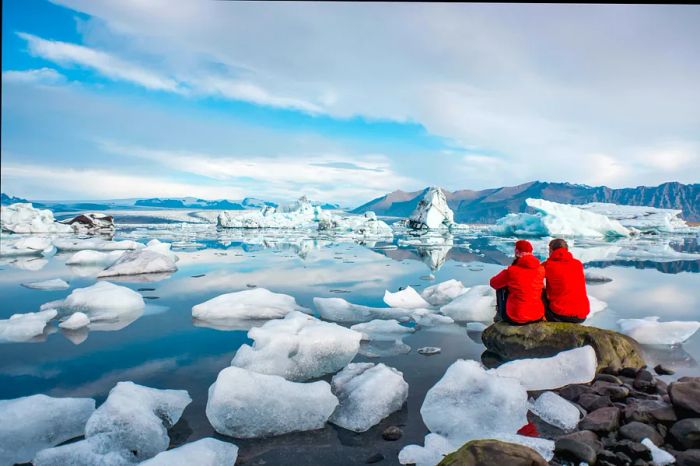 A couple enjoys the view from the edge of a lagoon teeming with icebergs