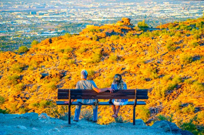 A couple relaxes on a bench at a viewpoint, basking in the sun over a dry landscape