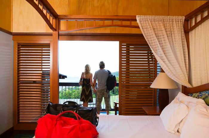 A couple stands together, holding hands, with their backs to the camera in a lodge hotel bedroom