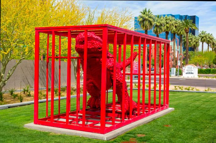 A red dinosaur inside a red cage on the grounds of an art museum