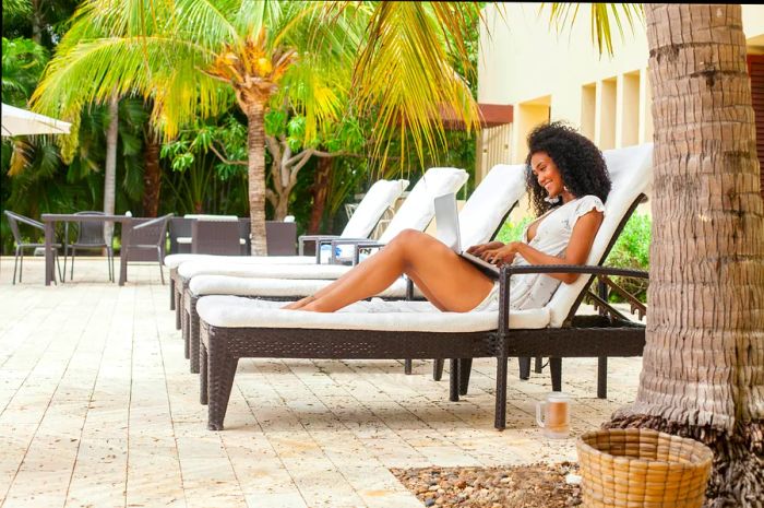 A woman relaxes on a pool chair in Colombia, working on her laptop amid lush tropical plants.