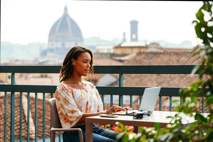 A black woman working on a laptop at a café in Florence, with the city’s rooftops visible in the background.