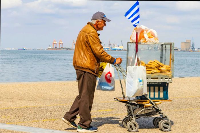 A vendor pushes a cart filled with koulouria rolls along the Thessaloniki waterfront, Macedonia, Greece